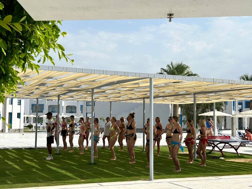 An animator leading a large outdoor dance class for guests wearing coin hip scarves