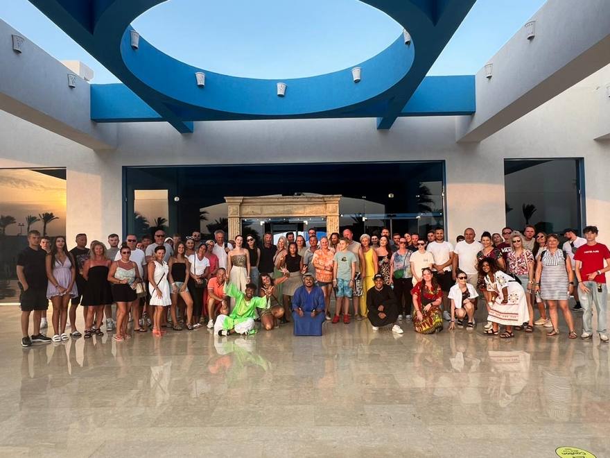 Guests and costumed animators posing together at the resort entrance at sunset